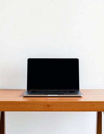 Laptop with blank screen on wooden table and white wall background.