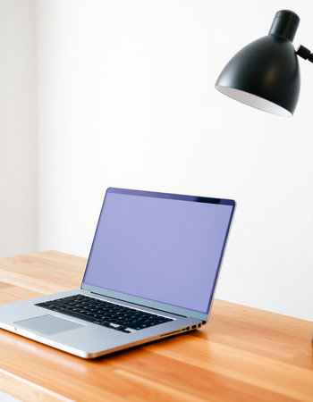 Laptop with blank purple screen on wooden table and lamp on white wall background