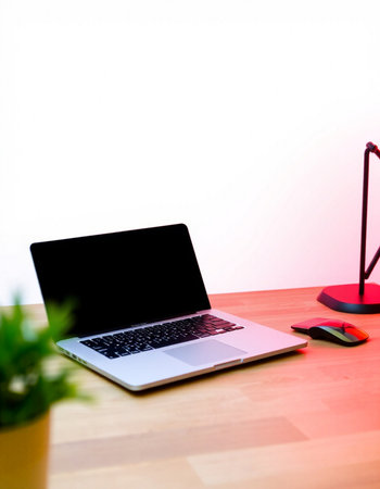 Laptop on a wooden table with a red lamp and a plant