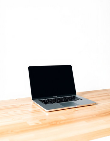 Laptop with blank screen on wooden table and white wall background.