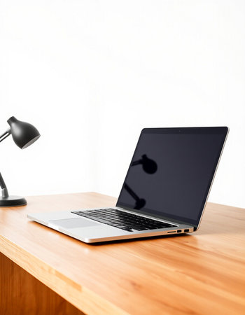 Laptop on wooden desk with lamp and white wall in the background