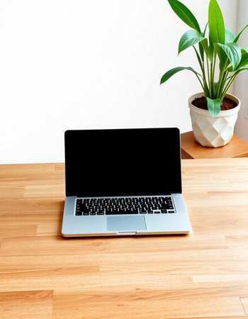 Laptop with blank screen on wooden table and white wall background.