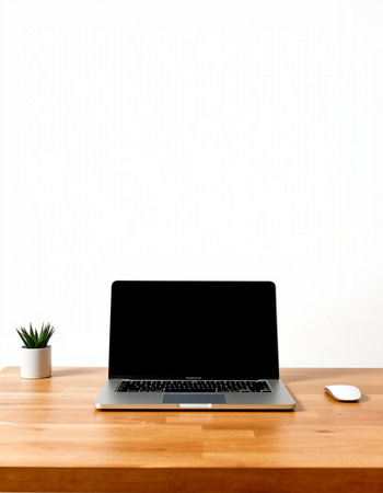 Laptop with blank screen on wooden desk and white wall background.