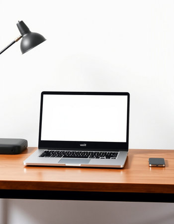Laptop with blank screen on wooden table with lamp and mobile phone