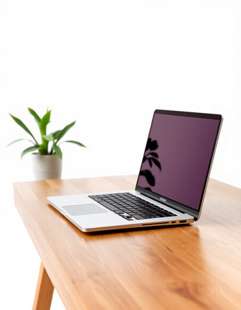 Laptop on a wooden table with a green plant in the background