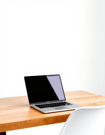 Laptop on wooden table with white chair and white wall background.