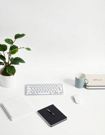 White office desk with keyboard, notepad, coffee cup, and plant.
