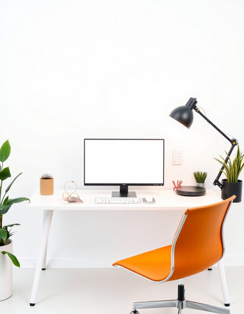 Modern workspace with blank screen computer and orange chair on white desk.の写真素材