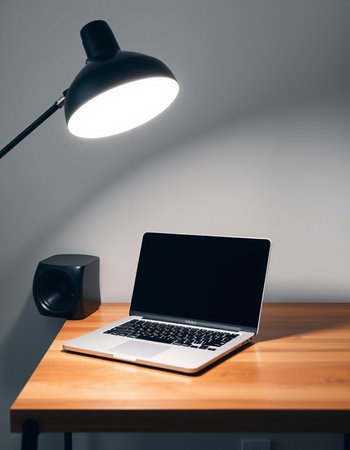 Laptop with blank screen on wooden table and lamp on grey wall background