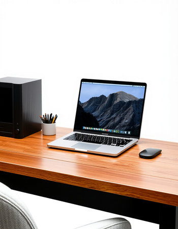 Laptop on a wooden desk in front of a white wall.