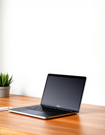 Laptop with blank screen on wood table and white wall background.