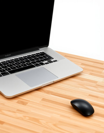 Laptop and mouse on a wooden table with white wall in the background