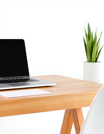 Laptop on wooden table with white wall and plant in the background