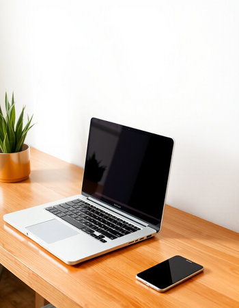 Laptop with blank screen on wooden table and white wall background.