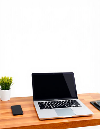 Laptop with blank screen and mobile phone on wooden desk with white wall background