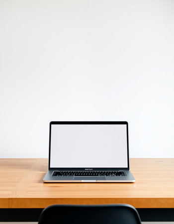 Laptop with blank screen on wooden table and white wall background.
