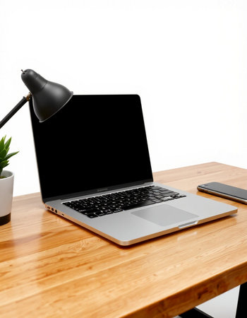 Laptop and office supplies on wooden table with white wall background.