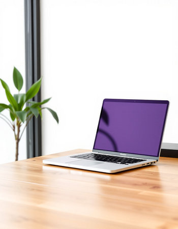 Laptop with purple screen on wood table and white wall background.