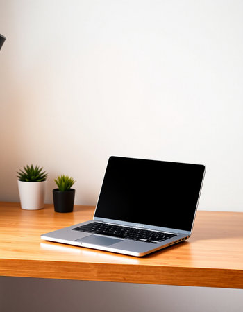 Laptop with blank screen on wooden table and white wall background.