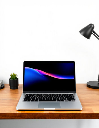 Laptop on wooden desk in front of white wall with lamp.