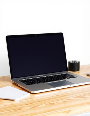 Laptop with blank screen on wooden table and white wall background.