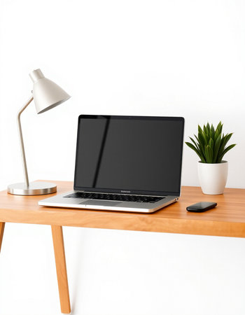 Laptop with blank screen on wooden desk with lamp and potted plant