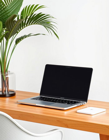 Laptop with blank screen on wooden table and white wall background.