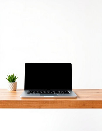 Laptop with blank screen on wooden table and white wall background.
