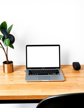 Laptop with blank screen on wooden desk and white wall background.
