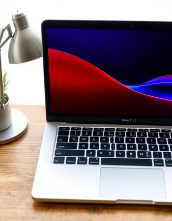 Laptop on wooden desk with colorful abstract design on screen.