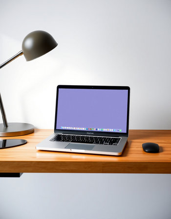 Laptop on a wooden table with a lamp and a mouse.の写真素材