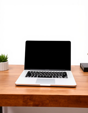 Laptop with blank screen on wooden desk with white wall background.