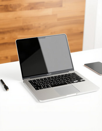 Laptop on a white table with a smartphone and a pen.