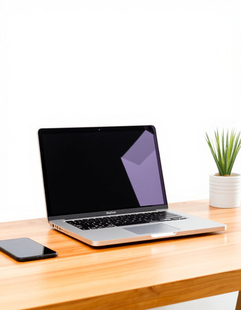 Laptop with blank screen on wooden table and white wall background.