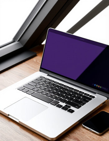Laptop with blank screen and smartphone on wooden table near window.