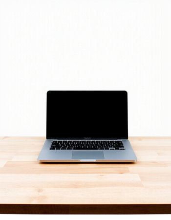 Laptop with blank screen on wooden table and white wall background.