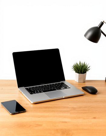 Laptop with blank screen on wooden table with black lamp and smartphone
