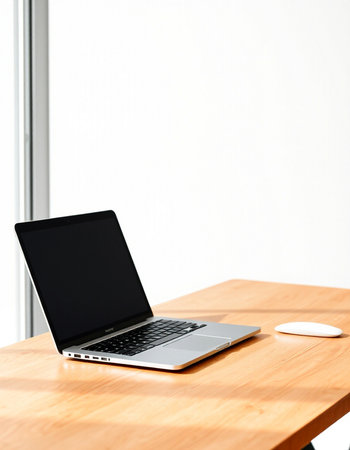 Laptop on a wooden table in front of a white wall.