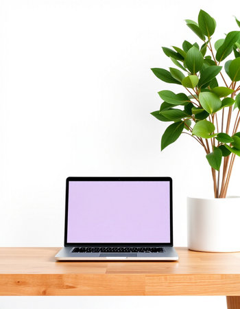 Laptop with blank purple screen on wooden table and green plant on white wall background