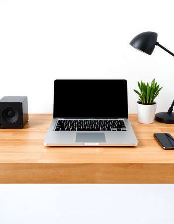 Laptop computer on wood desk with modern speaker and plant on white wall background