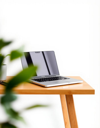 Laptop computer on wooden table with green plant on white wall background