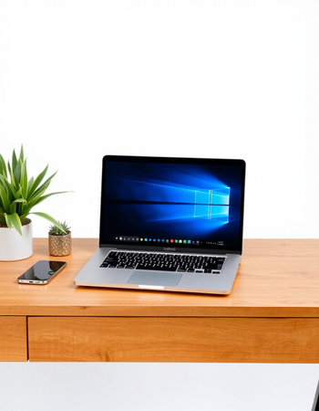 Laptop on wooden table with white wall and plant on the background
