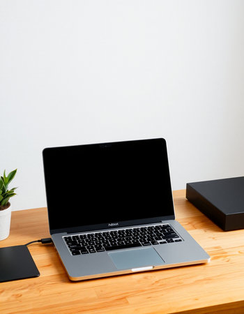 Laptop with blank screen on wooden desk and white wall background.