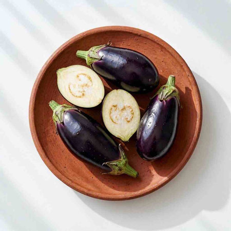 Fresh eggplants in a clay bowl on a white background.