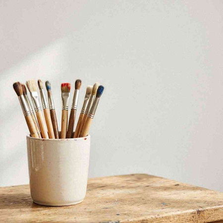 Paint brushes in a cup on a wooden table against a white wall