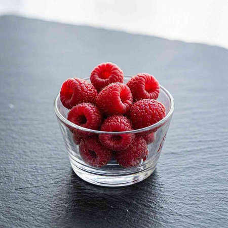 Fresh raspberries in a glass bowl on a black background.