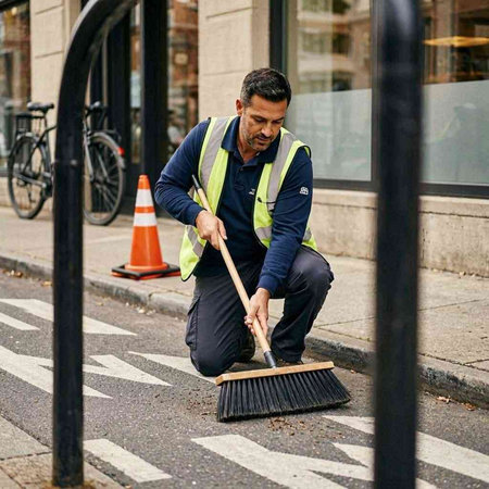Male worker cleaning the sidewalk with a broom in a city street.
