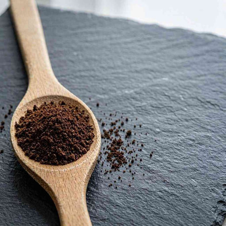 Ground coffee in a wooden spoon on a black background. Copy space.