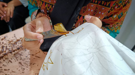 Close Up of a hand holding a Canting to make a motif on Indonesian traditional batik cloth