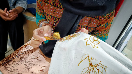 Close Up of a hand holding a Canting to make a motif on Indonesian traditional batik cloth
